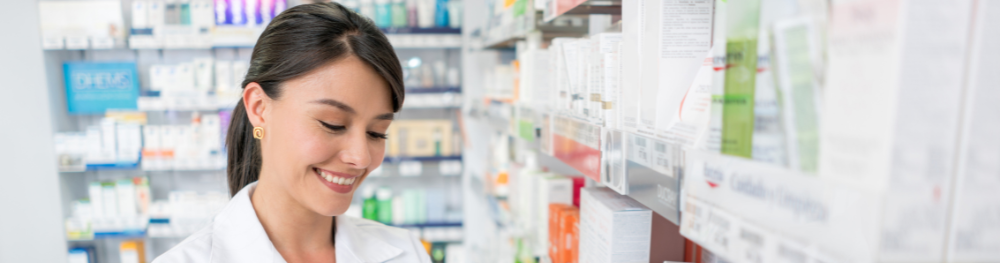 Pharmacist smiling behind a counter with shelves of medications